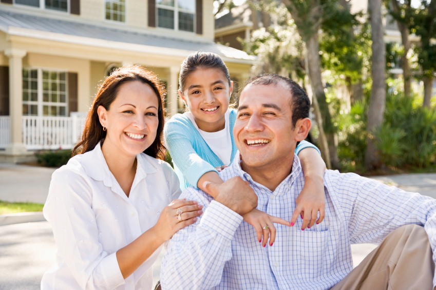 Portrait of happy Hispanic family with 9 year old girl sitting together with house in background