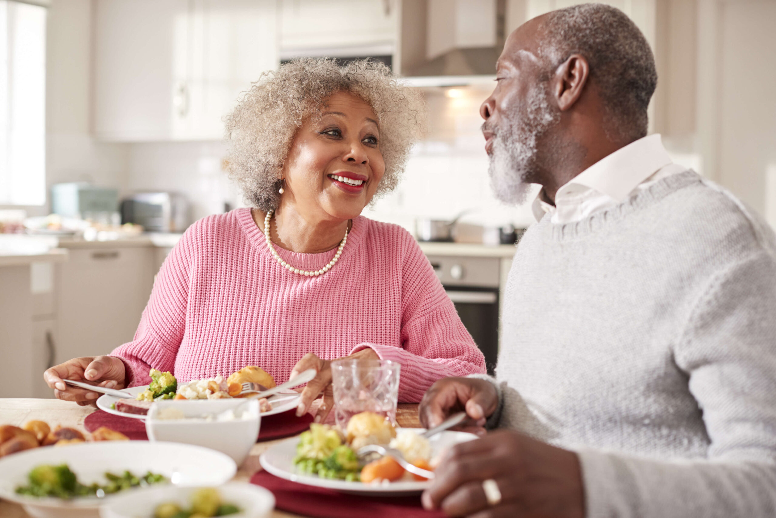 An elderly couple sharing a joyful meal together in a well-lit kitchen.